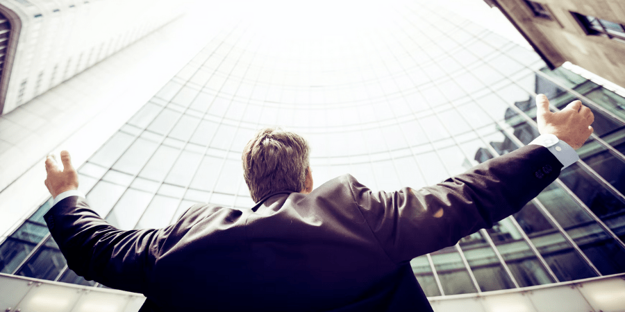 Man Holding Arms Up to Sky Infront of Office Building